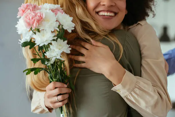 Portrait of two women hugging each other and holding flowers.