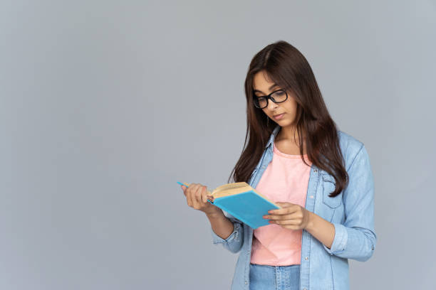 Serious focused indian young woman college university school student wear glasses hold read book isolated on grey studio background, teen girl prepare for exam study stand on gray wall copy space seria enfocada mujer india joven estudiante de la universidad estudiante de la universidad desgaste gafas mantener libro de lectura aislado en el fondo de estudio gris, chica adolescente prepararse para el examen de estudio stand en el espacio de copia de