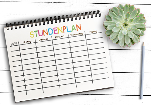 top view of class schedule or timetable template with German word STUNDENPLAN on notepad against rustic white wooden table