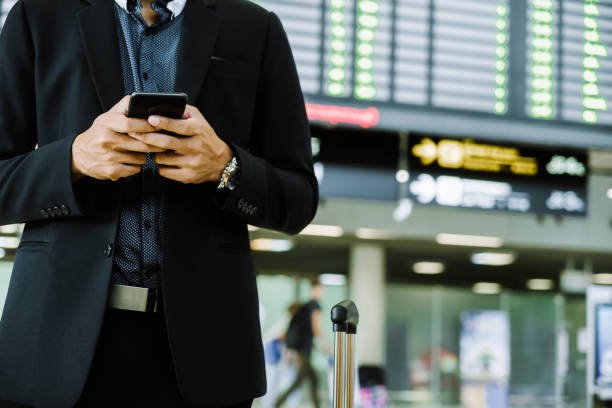 istock Businessman checking e-mail on mobile phone while walking with suitcase inside airport 1160036888