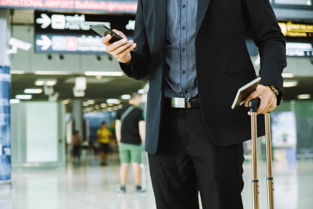 istock Businessman checking e-mail on mobile phone while walking with suitcase inside airport 1160036894