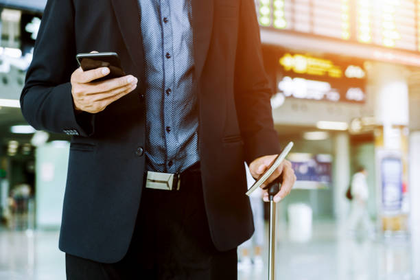 istock Businessman checking e-mail on mobile phone while walking with suitcase inside airport 1160036944