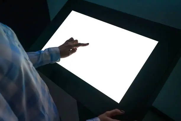 Photo of Woman touching interactive white blank touchscreen display kiosk at exhibition