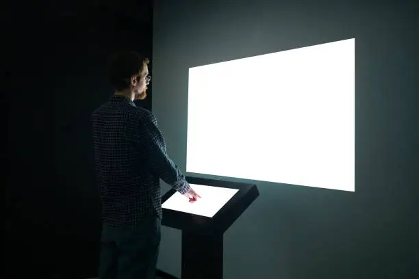 Photo of Man looking at white blank large interactive wall display - mockup image