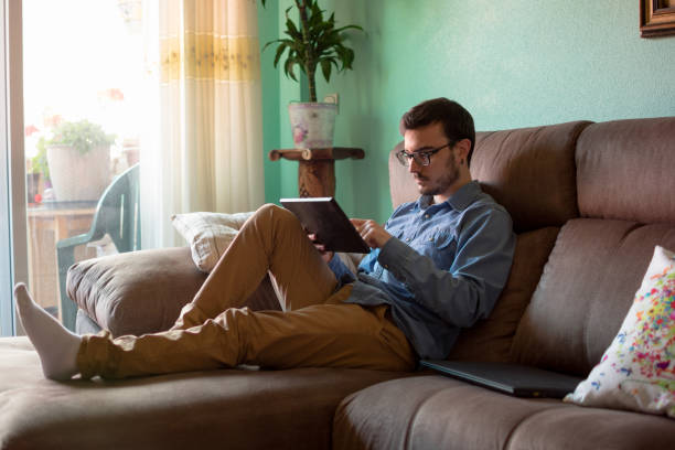 istock Young man with tablet on sofa at home 1160043644