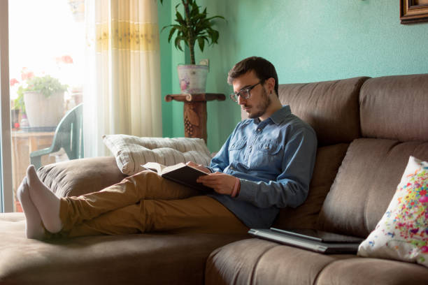 Portrait of young man with book on sofa relaxing at home. Reading, house.