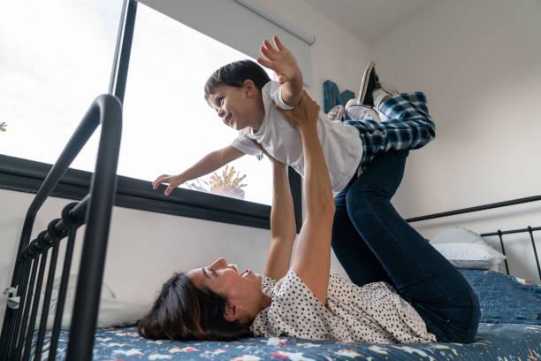 istock Mother lying down on bed carrying son simulating an airplane both having a lot of fun 1160046163