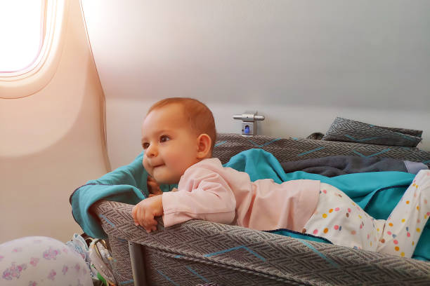 Happy infant baby lyes in special bassinet in airplane at his stomach. First flight of the baby, she is impressed and looking on mom stock photo