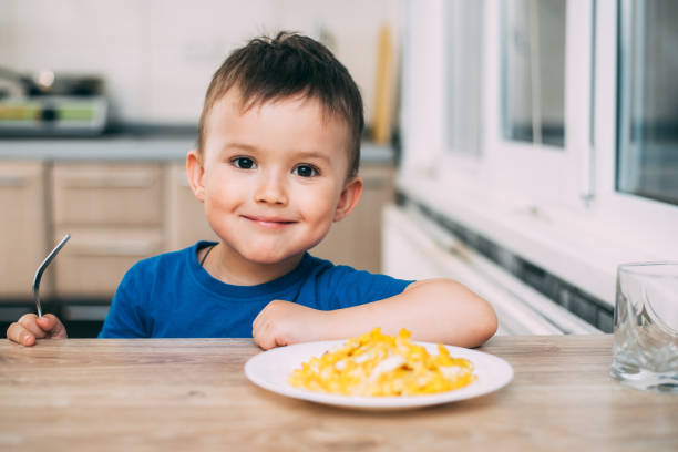 a child in a t-shirt in the kitchen eating an omelet, a fork