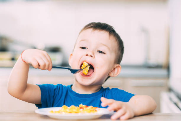 ein kind in einem t-shirt in der küche isst ein omelett, eine gabel - eierkuchen speise stock-fotos und bilder