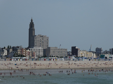 Bathers at the beach of Le Havre seen from Sainte-Adresse, Normandy, France.\nYou can see the beach huts and in the background the Church of St. Joseph, emblematic building of the reconstructed city center of Le Havre.
