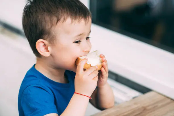 Photo of baby in blue t-shirt eating white bread and butter