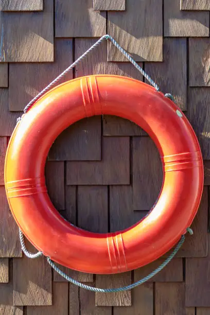 Orange lifebuoy/lifebelt emergency equipment device hanging on floating water boat house/ home exterior deck wall. Drowning overboard incident safety standard gear.