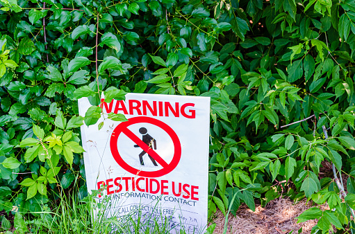 Warning Pesticide Use Sign in front of bushes in a publci park