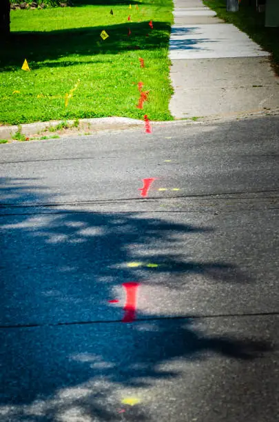 Photo of Red & yellow markers for underground utilities across a road and on a lawn next to a sidewalk