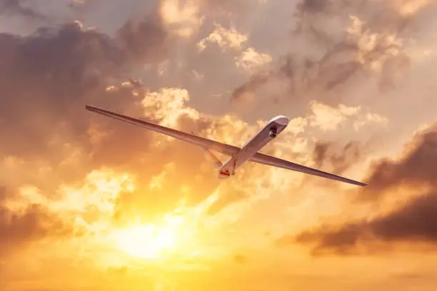 Photo of Unmanned military drone flies the at sunset clouds sky.