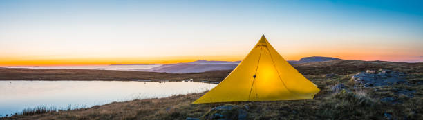 istock Warmly illuminated mountain tent overlooking misty lake ridges panorama sunrise 1160060468