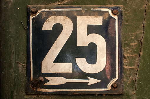Weathered grunge square metal enameled plate of number of street address with number 25 closeup