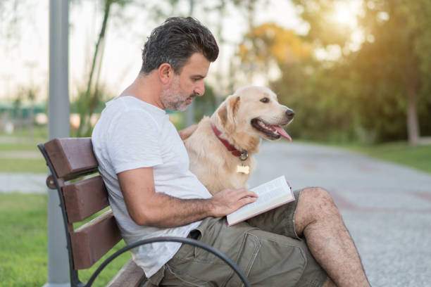 istock Man reading book with his dog on the park bench 1160085765