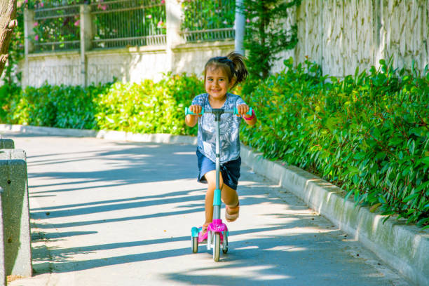 3 anos de menina velha monta o scooter entre árvores - preschool 2 3 years preschooler little girls - fotografias e filmes do acervo