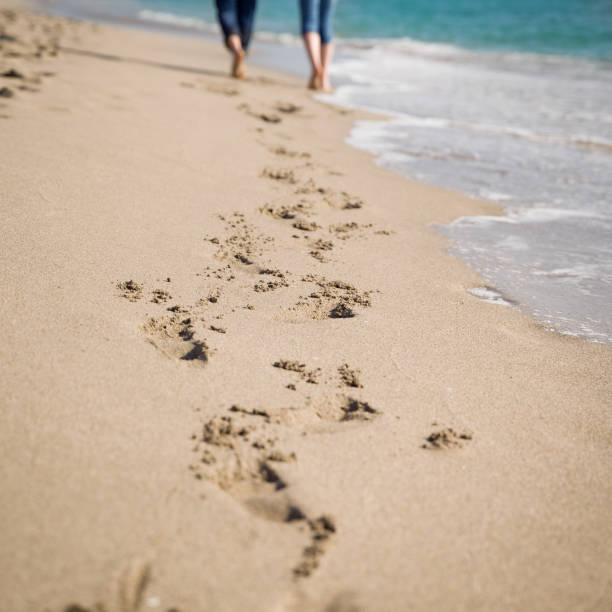 istock Happy young couple walking along empty beach. Fresh footprints on the ocean shore. Selective focus. 1160094182
