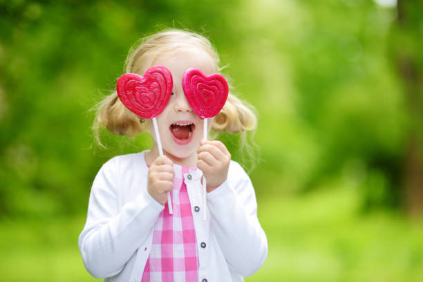 美しい夏の日に屋外で巨大なハート型のロリポップを食べるかわいい女の子 - child valentines day candy eating ストックフォトと画像