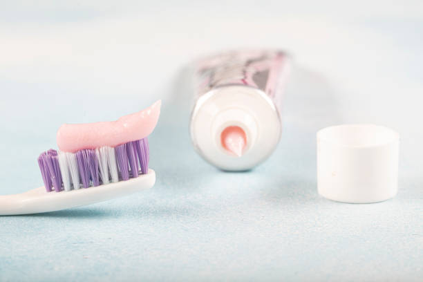 Toothbrush with pink toothpaste next to a tube of toothpaste against blue background