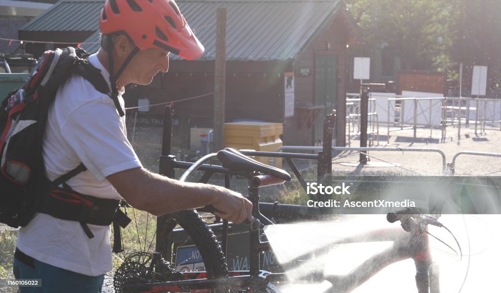 Mature mountain biker cleans bike at bike wash station He is backlit in the spray 55-59 Years Stock Photo
