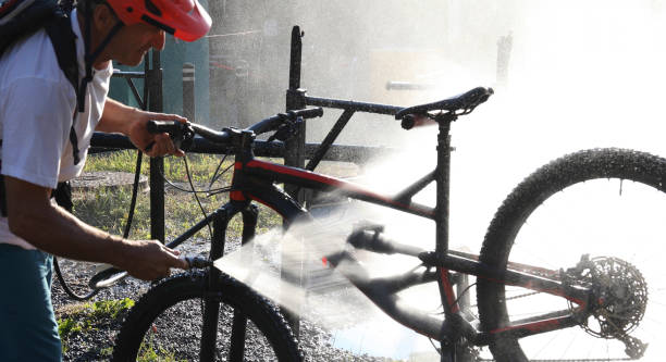 Mature mountain biker cleans bike at bike wash station He is backlit in the spray backpack sprayer stock pictures, royalty-free photos & images