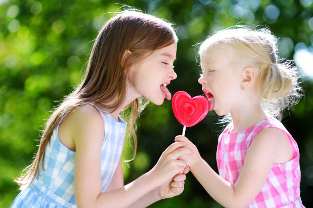 屋外で巨大なハート型のロリポップを食べる2人のかわいい妹 - child valentines day candy eating ストックフォトと画像