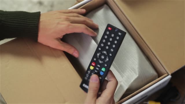 Male Hands Opening Carton Box With Tv Decoder Controls.