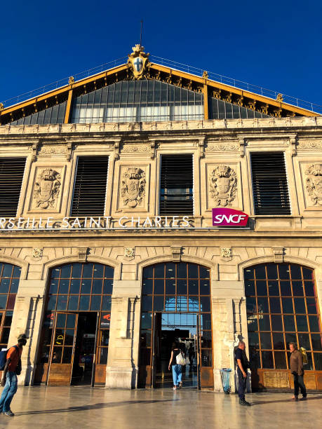 Marseille, France: Marseille Saint Charles Train Station at Dusk Marseille, France: A police officer chats with a barefoot man as a traveler enters the sunlit Marseille Saint Charles train station at dusk (golden hour). The station dates from 1926. 1926 stock pictures, royalty-free photos & images