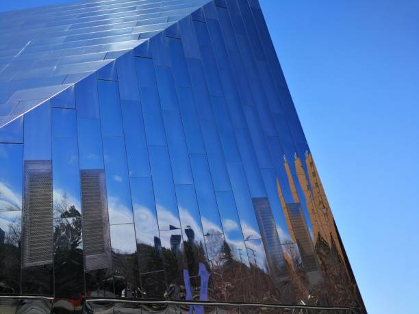 istock Buildings, trees, white clouds, and blue sky reflecting off modern glass structure 1160120423