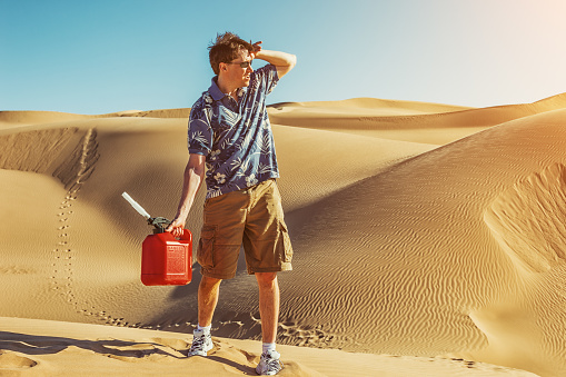 Photo of a man hiking through desert dunes with a gas can, in search of fuel.