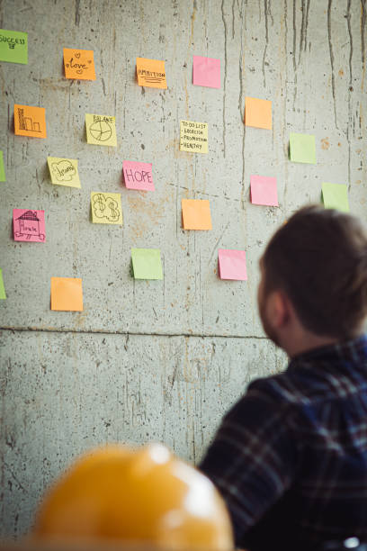 istock Back of engineer sitting in office and look at colorful sticky message on cement wall. Work lifestyle concept. 1160122066