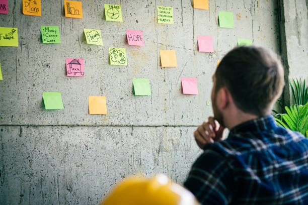 istock Back of engineer sitting in office and look at colorful sticky message on cement wall. Work lifestyle concept. 1160122084