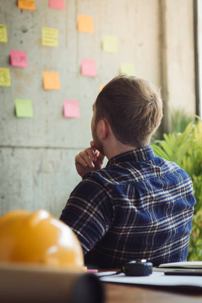 istock Back of engineer sitting in office and look at colorful sticky message on cement wall. Work lifestyle concept. 1160122085