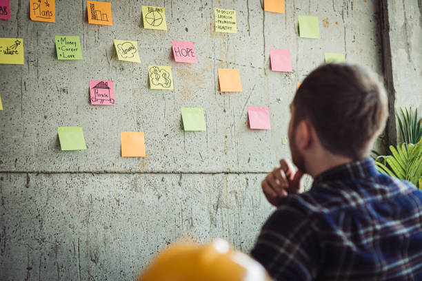 istock Back of engineer sitting in office and look at colorful sticky message on cement wall. Work lifestyle concept. 1160122086