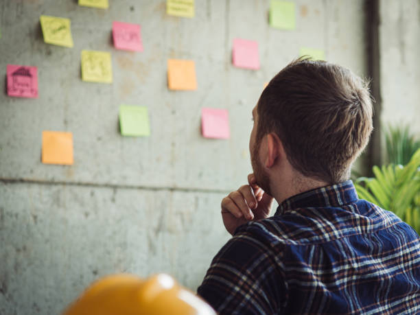 istock Back of engineer sitting in office and look at colorful sticky message on cement wall. Work lifestyle concept. 1160122087