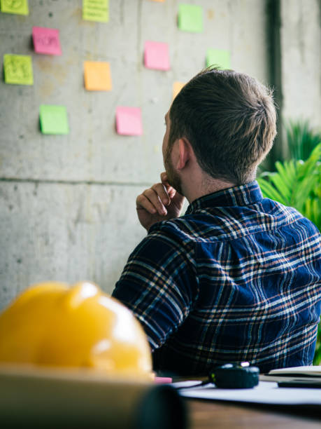 istock Back of engineer sitting in office and look at colorful sticky message on cement wall. Work lifestyle concept. 1160122110