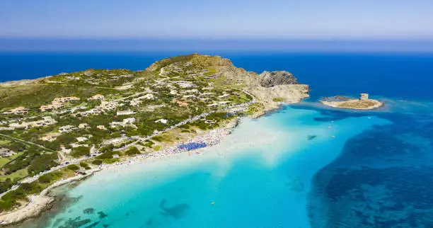 Stunning aerial view of the Spiaggia Della Pelosa (Pelosa Beach) full of colored beach umbrellas and people sunbathing and swimming in a beautiful turquoise clear water. Stintino, Sardinia, Italy.