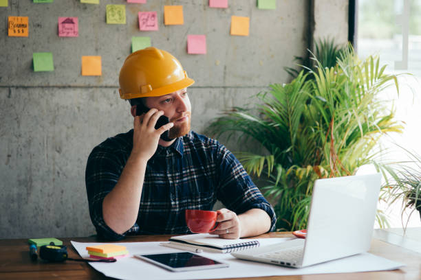 istock Engineer talking with phone and drinking coffee in office, colorful sticky notes on cement wall background. 1160135536