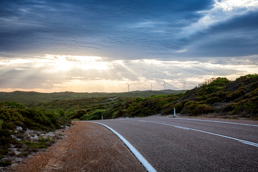 A stunning sunset on the coast of Esperance Western Australia with wind turbines and sun rays through the clouds.