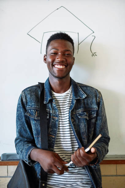Graduation is the goal Portrait of a happy young man standing in front of a whiteboard with an illustrated graduation cap at university graduation man stock pictures, royalty-free photos & images