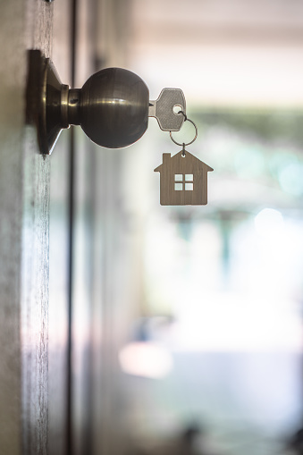 House key with home keyring in keyhole on wood door, copy space