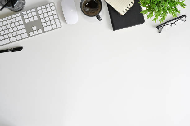 istock Top view office table desk. Workspace with blank computer keyboard and office supplies, green leaf, and coffee cup on white Top table. 1160149431
