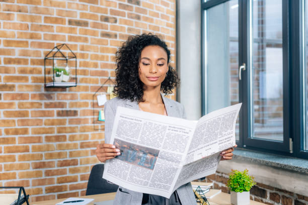 atractivo afroamericano casual mujer de negocios leyendo periódico de negocios en oficina de loft - mujer leyendo periodico fotografías e imágenes de stock