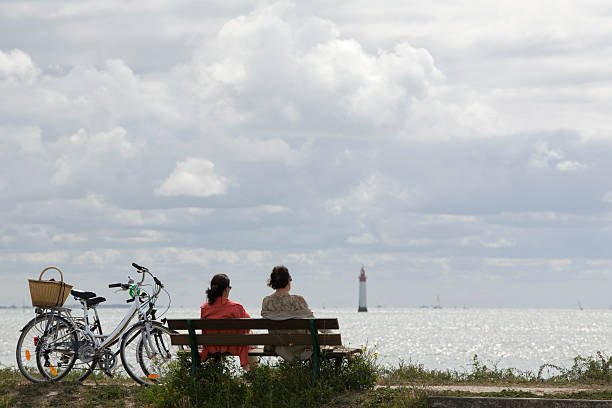 two woman on a bench looking at the lighthouse stock photo