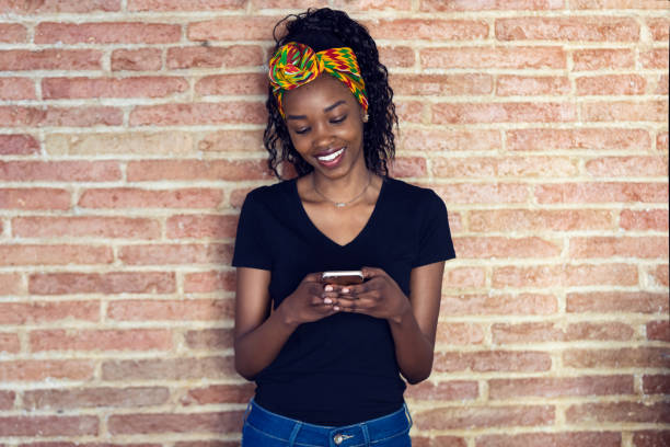 istock Happy young woman using her mobile phone while standing in front of a wall. 1160177273