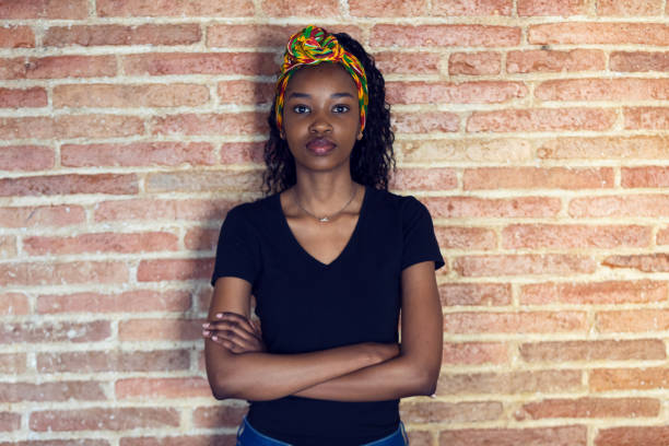 istock Serious young woman looking at camera with arms crossed while standing in front of a wall. 1160177478